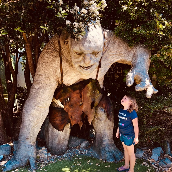 traveler Harper standing under a towering troll statue at Wētā Cave in Wellington, New Zealand, exploring the magical world of movie-making and special effects during a family adventure.