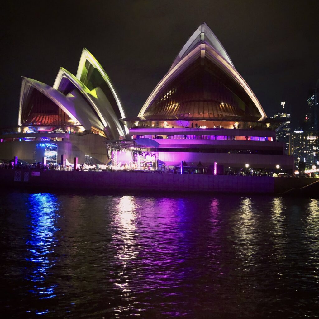 Iconic Sydney Opera House glowing at night on New Year’s Eve, framed by fireworks and vibrant harbor reflections during Australia’s world-famous celebration.