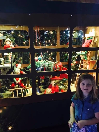 Harper standing in front of a festive elf workshop display filled with animated elves, toys, and twinkling lights at Smith & Caughey’s in Auckland, New Zealand.