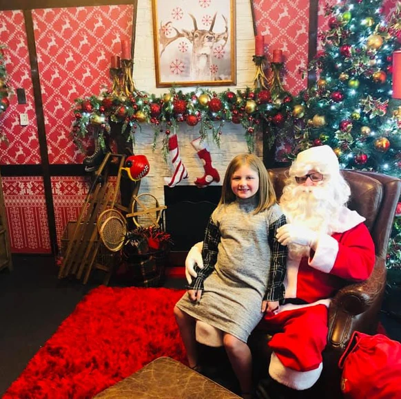 Harper sitting on Santa’s lap in a festively decorated room with Christmas trees, stockings, and holiday toys at Smith & Caughey’s in Auckland, New Zealand.