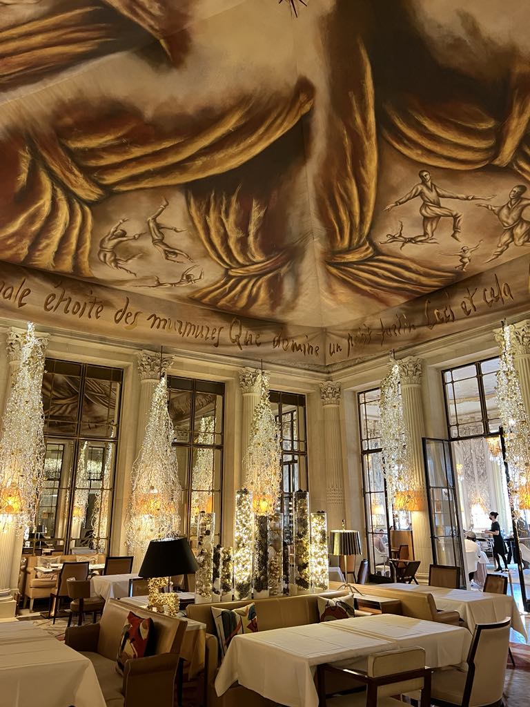 Whimsical ceiling art featuring sculpted hands as part of the striking interior decor at Le Meurice restaurant in Paris, blending classic elegance with contemporary surrealism in a luxury dining setting.