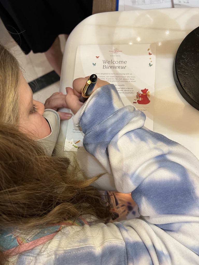 Kidntraveler Harper filling out a welcome card at a luxury hotel, engaging in a thoughtful and interactive guest experience during a family stay in Paris.