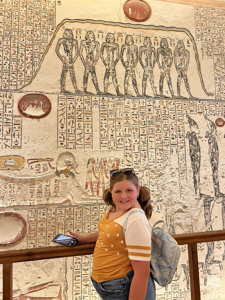 a girl standing in front of a wall with egyptian hieroglyphics