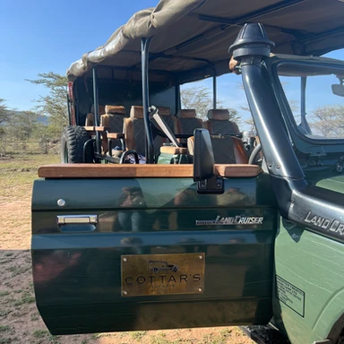 Luxury safari jeeps from Cottar’s 1920s Camp in Kenya, set against the scenic backdrop of the African wilderness during a family adventure.