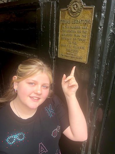 Teen traveler in London pointing to the "Texas Legation" sign, discovering unique U.K.-Texas historical connections on a family adventure.