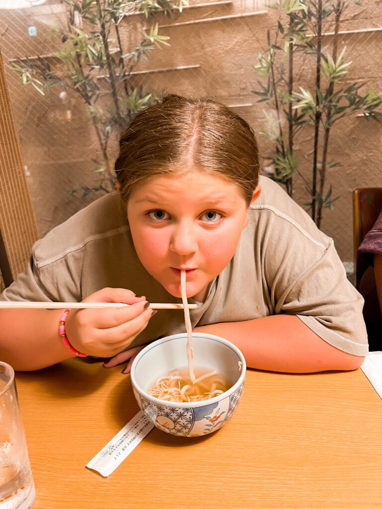Harper enjoying a warm bowl of noodles food with chopsticks during her culinary adventures in Japan. Slurping up the flavors one bite at a time!