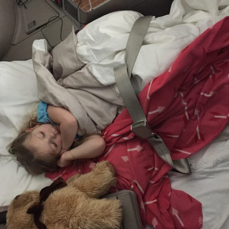 kid traveler Harper resting in a lie-flat first class seat, enjoying luxury comfort and privacy during an international flight.
