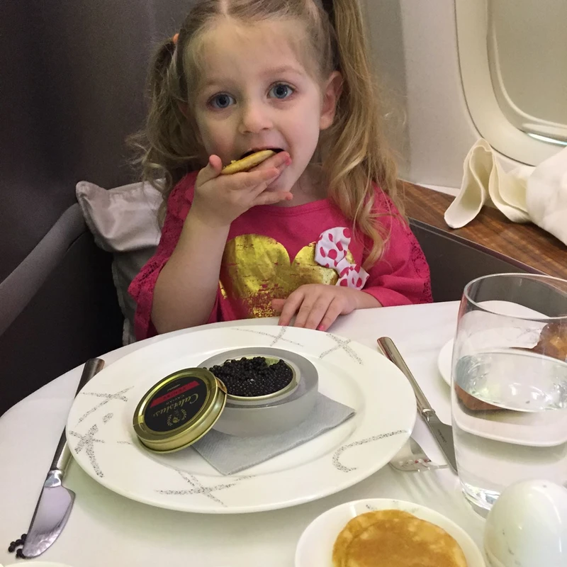 kid traveler Harper savoring caviar in Cathay Pacific first class, experiencing luxury in-flight dining during a premium international family journey.