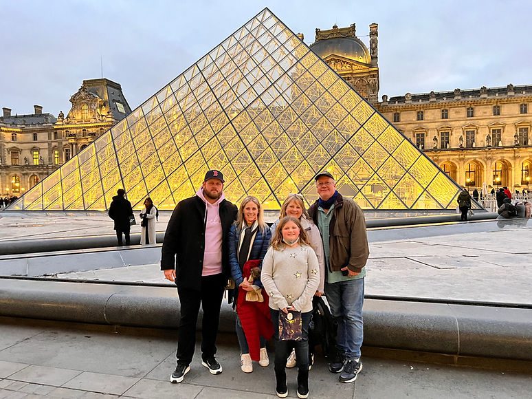 Family travel moment in Paris with teen explorer Harper, her family, and their guide standing in front of the iconic Louvre Museum during a European adventure.