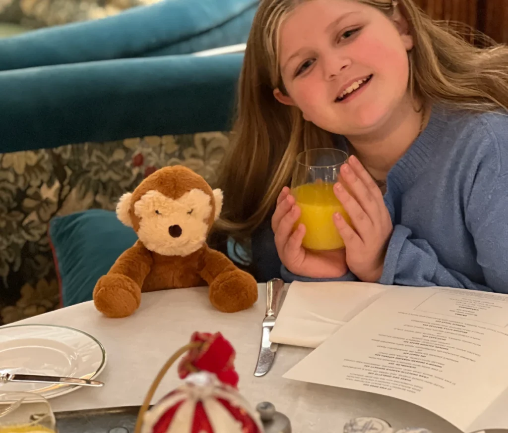 Harper enjoying breakfast with her plush monkey Albee at The Brown’s Hotel in London, sipping orange juice.