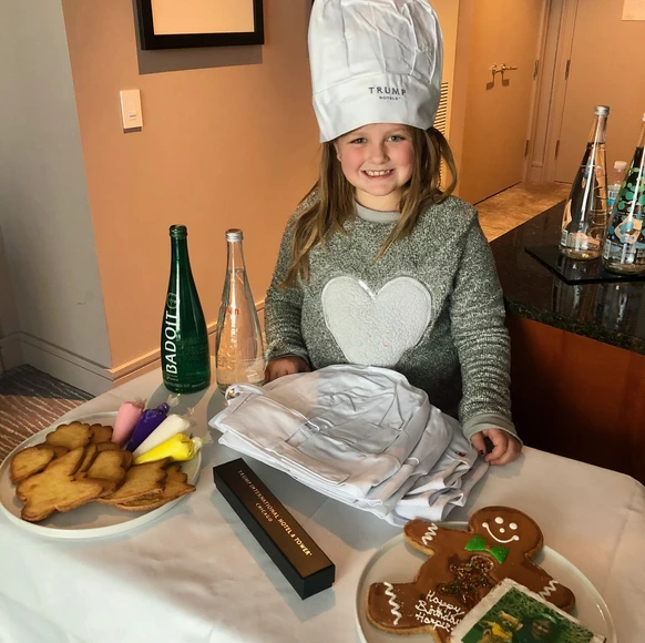 traveler Harper wearing a chef hat and smiling with a festive cookie decorating kit left as a holiday surprise in her Trump Hotel Chicago suite during a luxury family stay.
