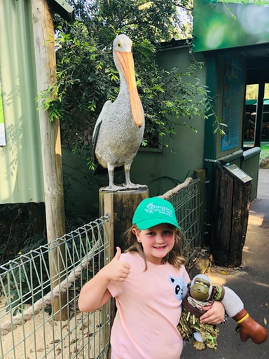 kid traveler Harper giving a thumbs up while wearing a Featherdale Wildlife Park hat, celebrating her fun wildlife adventure in Sydney, Australia.