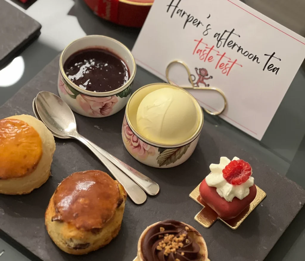 Harper’s afternoon tea tasting with scones, clotted cream, jam, and elegant pastries on a slate platter.