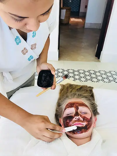 A spa therapist gently applies a chocolate facial mask to Harper’s face at Mukul Resort in Nicaragua. Harper is relaxing on a spa bed with her eyes closed and a calm expression.