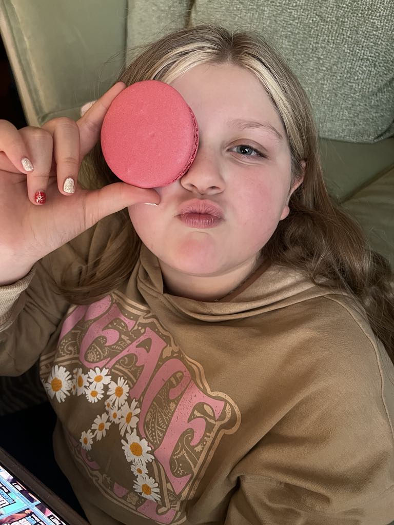 Teen traveler Harper being cheeky with a macaron held up to her eye and a kissy face, capturing a playful and sweet moment during a luxury family stay in Geneva Switzerland