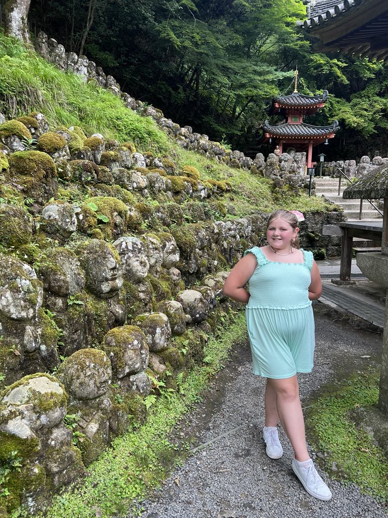 Teen traveler Harper exploring a sacred hillside filled with hundreds of stone Buddha head statues in Kyoto, Japan—an unforgettable moment of cultural and spiritual discovery during a family adventure.